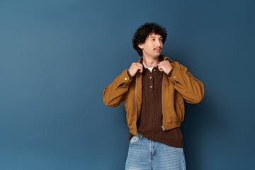 Stylish young man adjusting his jacket against a solid blue background in a modern setting