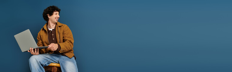 Stylish young man enjoys creativity while working on laptop against a vibrant blue backdrop © LIGHTFIELD STUDIOS