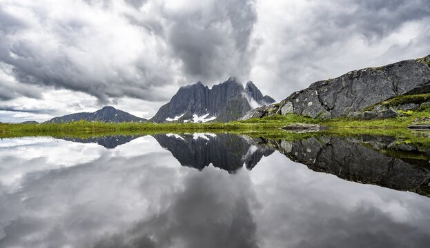 Small lake in mountain landscape, hike to Mount Barden, reflection with mountain peak Breidtind, Senja, Norway