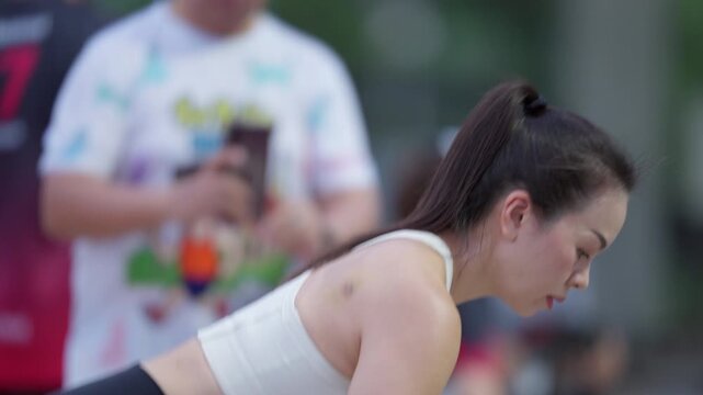 Side view of Asian woman doing bent-over row with weight plate during outdoor training. Strength, fitness, and body control in motion.