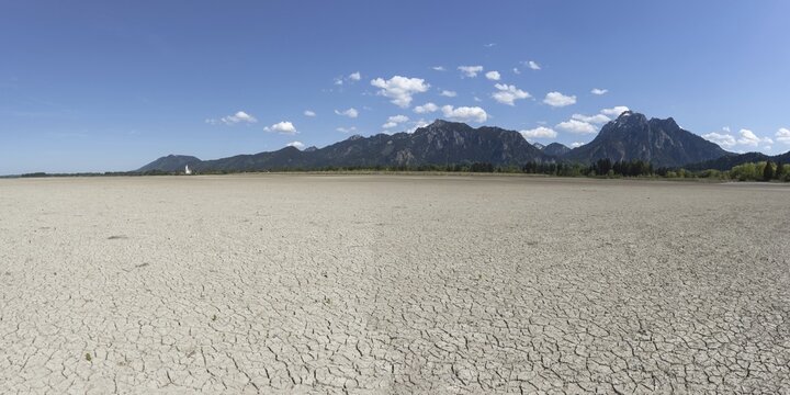 Cracked, dried out ground, waterless Forggensee in spring, behind it Tegelberg massif and S&auml;uling, Ammergau Alps, near F&uuml;ssen, Ostallg&auml;u, Bavaria, Germany