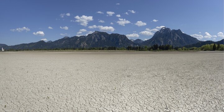 Cracked, dried out ground, waterless Forggensee in spring, behind it Tegelberg massif and S&auml;uling, Ammergau Alps, near F&uuml;ssen, Ostallg&auml;u, Bavaria, Germany