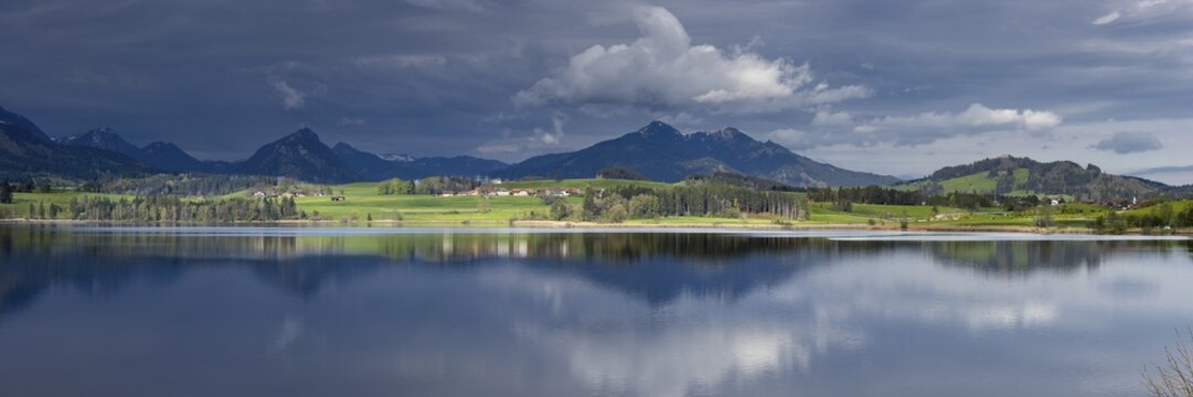 Panorama at sunrise over Lake Hopfensee to the sunlit western shore with farms, behind it receding thunderclouds, Lake Hopfensee, Ostallg&auml;u, Allg&auml;u, Bavaria, Germany