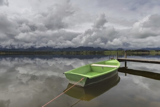 Storm clouds at sunset, a green rowing boat lashed to the wooden jetty, Hopfensee, Hopfen am See, near F&uuml;ssen, Ostallg&auml;u, Allg&auml;u, Bavaria, Germany