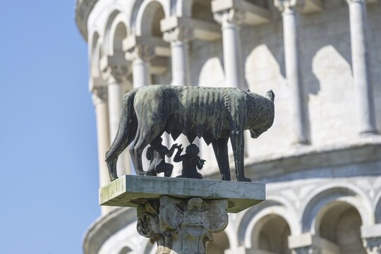 Capitoline she-wolf (lat. Lupa Capitolina), behind her the Leaning Tower of Pisa, Tuscany, Italy