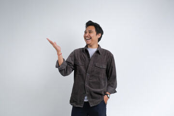 A cheerful young man in a brown shirt smiling and gesturing with open hand as if presenting or showing something, isolated on plain background.	