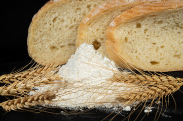 Freshly baked bread and wheat flour with stalks on a dark surface