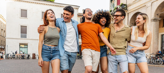 Happy multiracial group of friends walking on city street - Cheerful young people hanging outside...