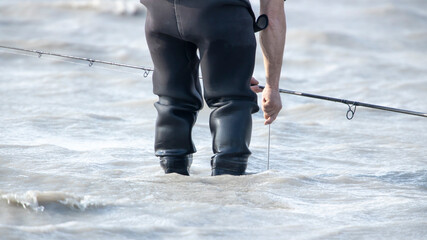 Angler in Watthose beim Fischen – Freizeitfischer im Wasser mit Angelrute, Symbol für Geduld,...