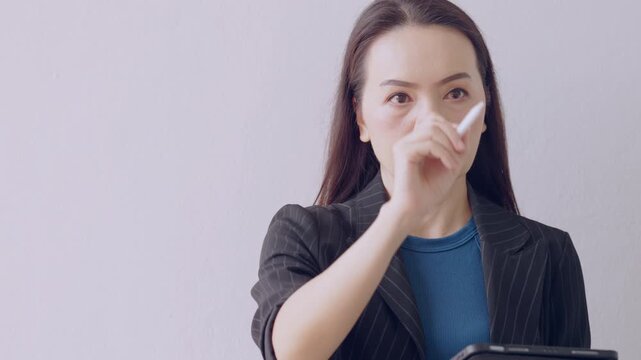 Asian businesswoman holding stylus in office with serious expression, symbolizing digital strategy and control.