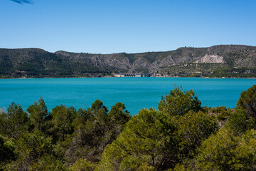 Fototapeta premium Scenic view of turquoise lake surrounded by mountains and greenery on a clear sunny day