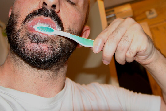 Hombre con barba lav&aacute;ndose los dientes con cepillo verde y pasta dent&iacute;frica para evitar sarro, caries, gingivitis, periodontitis y otras enfermedades dentales