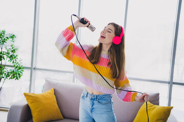 Charming woman singing passionately into a microphone while enjoying music at home, wearing a...