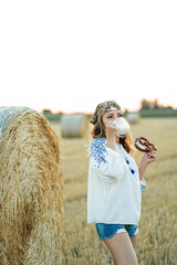 Woman 40s years old in a field with hay bales is enjoying the evening, drinking milk and eating...