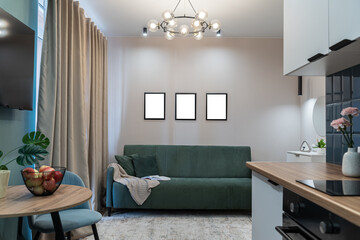 design of modern small living room. blue sofa with soft pillows and plaid, paintings on wall, thick curtains on window, and stylish chandelier on ceiling. Modern flat. Illuminated by lamp.