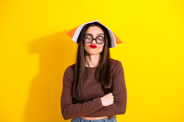 Playful young woman in glasses with book hat and trendy casual brown outfit posing against vibrant...