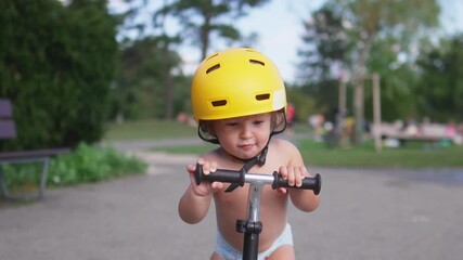 Toddler riding scooter wearing yellow helmet while practicing balance and steering skills, showing focus, determination, and early motor development outdoors