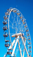 White Ferris wheel with glass cabins and moon, low-angle shot
