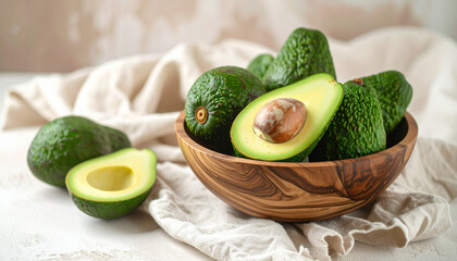 Close-up shot of a wooden bowl filled with fresh green avocados, some whole and some halved.