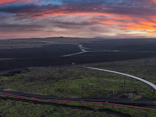 Expansive lava fields in Iceland with green moss, a winding road marked by a red barrier, and a...