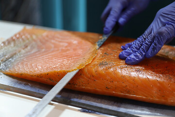 chef experto en corte de pescado, cortando un filete de salm&oacute;n ahumado fresco con un cuchillo especial de pescado
