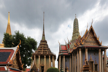 Fototapeta premium Temple roofs at Grand Palace, Bangkok - A wide shot of the ornate and majestic rooftops of the Grand Palace, showcasing traditional Thai architectural design under a cloudy sky.