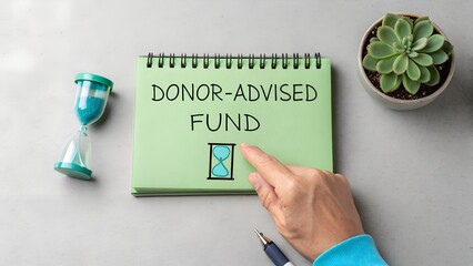 Green notebook with DONOR-ADVISED FUND text and hourglass illustration on gray surface – Charitable giving and timed philanthropy, business, finance, abstract, donation, nonprofit