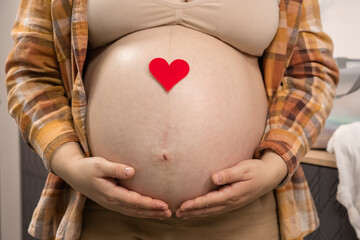 Pregnant woman holding red heart shape and feel love for unborn baby in belly. Awaiting for baby....