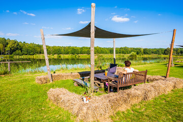 Female tourist resting at recreational areas with picnic furniture on lake shore in summer, Roztocze region, Poland
