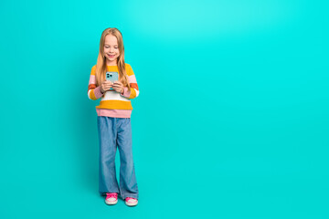 Adorable young girl using smartphone on turquoise background showing happiness and fashion in...