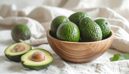 Close-up shot of a wooden bowl filled with fresh green avocados, with two halves in front.