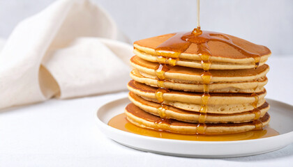 A stack of golden pancakes on a white plate, with syrup being poured over them.