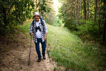 Obraz premium Cheerful senior man with backpack and hiking pole enjoying hiking in nature. 