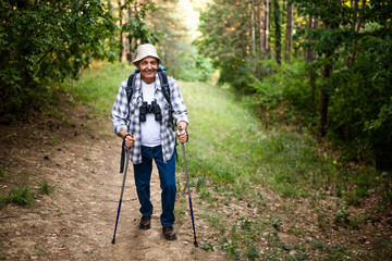 Obraz premium Active and happy senior man with backpack and hiking pole enjoying hiking in nature. 