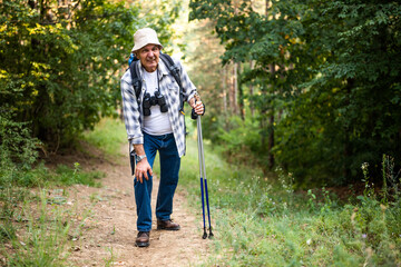 Senior hiker is struggling with knee injury or muscle strain while standing in forest during hiking.