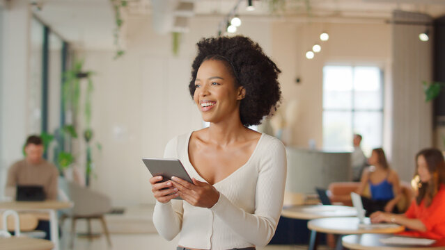 Businesswoman Standing In Modern Open Plan Office Using Digital Tablet
