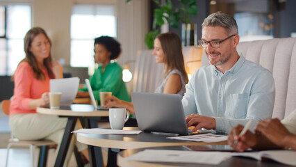 Mature Businessman Working On Laptop In Informal Seating Area Of Modern Office
