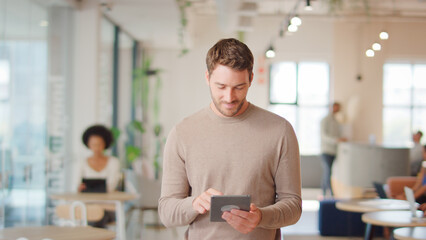 Businessman Standing In Modern Open Plan Office Using Digital Tablet