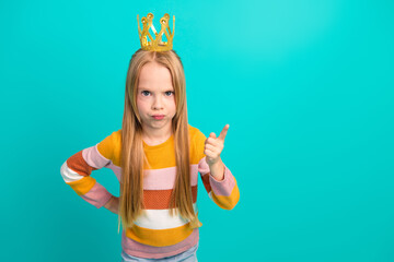 Cute young girl gesturing with a stern expression wearing a crown and a trendy striped shirt on a...