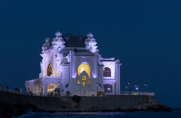 The stunning Constanta Casino in Romania, beautifully lit at dusk. The building is a prominent example of Art Nouveau architecture, with its ornate, shell-like facade glowing in the deep blue twilight