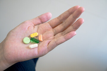 An individual holding a daily dose of assorted medications, colorful vitamin tablets, and nutritional supplements in their open palm, illustrating a personal healthcare regimen