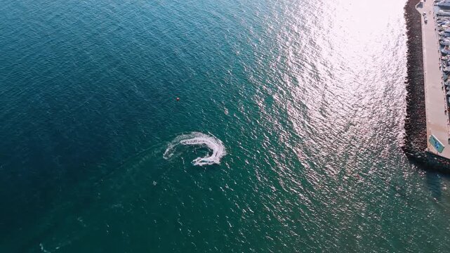 Watercraft maneuvers in coastal waters. A watercraft makes a sharp turn in clear coastal waters, with a marina visible in the sunny background.