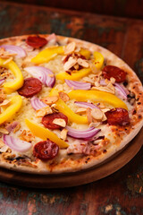 Pizza with chorizo ​​sausage, mozzarella cheese and yellow pepper. Rustic wooden background. Soft focus.	