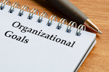 Close up notepad with the words Organizational Goals written on lined paper lying flat on a desk.