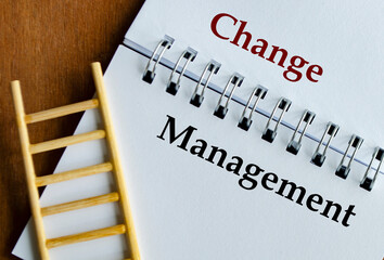 Notepad displaying Change Management in bold text with ladder on wooden surface.