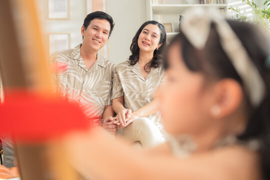 Happy Asian family spending quality time together at home. Father and daughter drawing on the floor with colored pens while mother works on a digital tablet smartphone on the sofa. Warm, modern living
