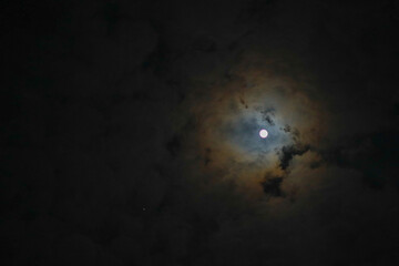 Rainbow-colored clouds surround the moon in the night sky.