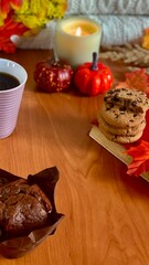 A cozy setting features a cup of coffee beside delicious cookies and a chocolate treat, surrounded by small pumpkins and fall leaves, perfect for autumn enjoyment