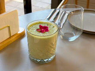 Glass of green matcha drink with edible flower. Refreshing beverage, garnish and modern presentation in cafe setting.