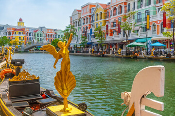 Decorative golden statue on gondola floating in canal lined with colorful Mediterranean style buildings on Phu Quoc island, Vietnam, with cafes, shops and trees. Grand world city. Italian architecture © samael334
